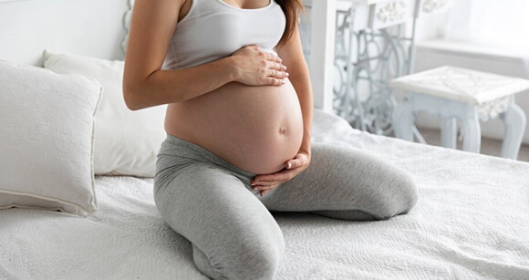 Mulher grávida sentada na cama com as mãos na barriga Mulher grávida sentada na cama com as mãos na barriga