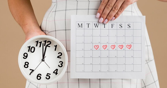 Mulher segurando relógio e calendário, gerenciando o seu período fertil Mulher segurando relógio e calendário, gerenciando o seu período fertil