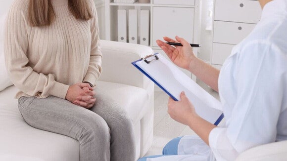 Médica com uma prancheta e uma caneta nas mãos sentada diante de uma paciente mulher, explicando os sinais do período fértil Médica com uma prancheta e uma caneta nas mãos sentada diante de uma paciente mulher, explicando os sinais do período fértil