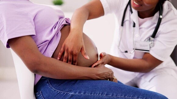 Uma profissional de saúde examina a barriga de uma gestante sentada. Uma profissional de saúde examina a barriga de uma gestante sentada.