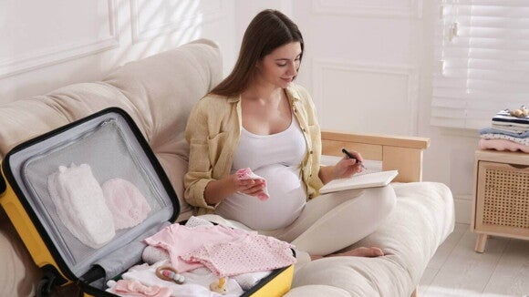 gestante preparando mala de maternidade enquanto faz anotações. gestante preparando mala de maternidade enquanto faz anotações.