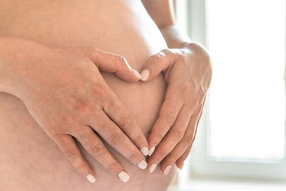 Gestante com as mãos sobre a sua barriga formando um coração