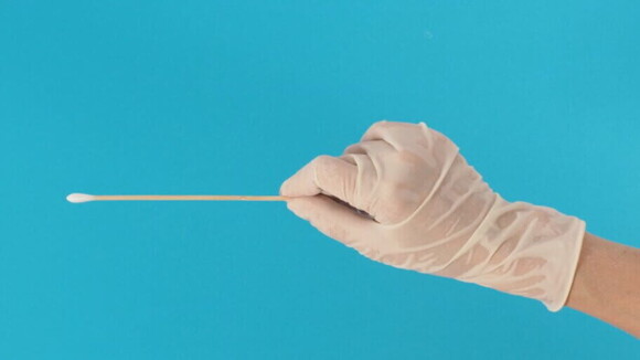 Mão com luva médica segura um cotonete sobre um fundo azul Mão com luva médica segura um cotonete sobre um fundo azul
