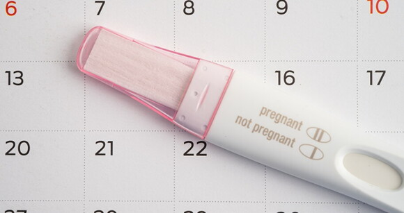Um teste de grávidez branco e rosa colocado sobre um calendário Um teste de grávidez branco e rosa colocado sobre um calendário